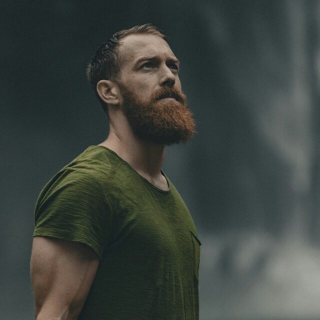 Muscular man with orange beard and green t-shirt looking upwards